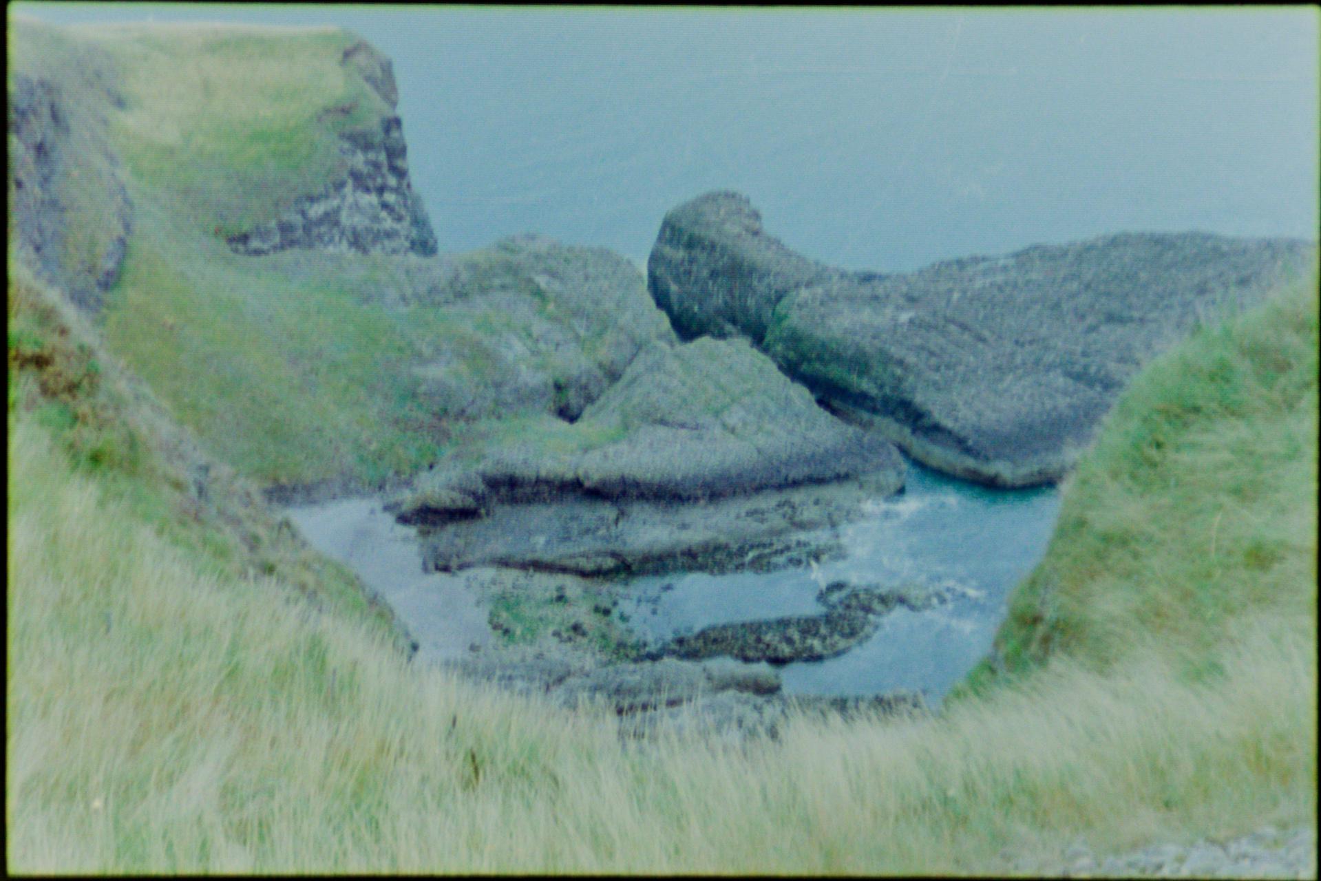 A picture of a bay and some big rocks, caught between a bank of grass
